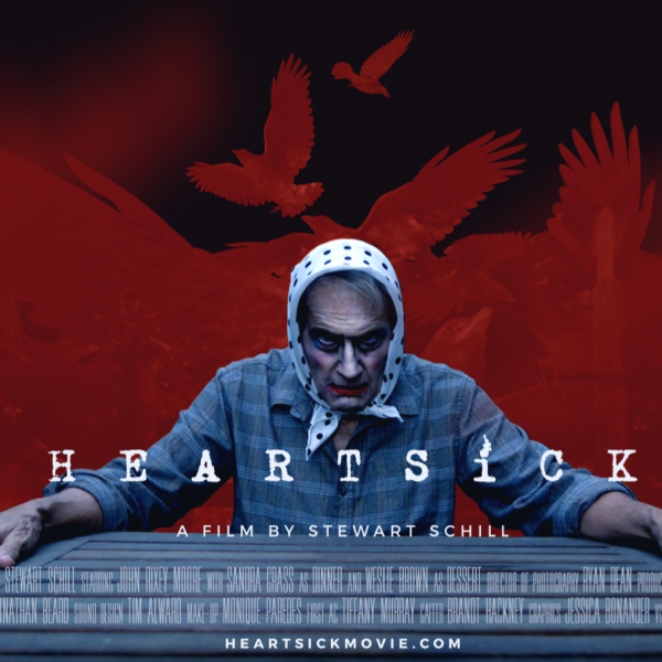 A man wearing make up and a headscarf grips a table, a red and black background with shadowed birds fly behind him